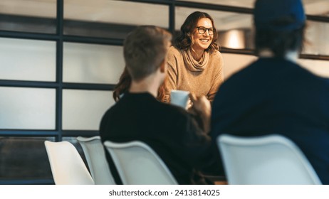 Group of colleagues engages in a dynamic discussion. A confident woman leads the team, presenting ideas to attentive businessmen and women. Their collaboration drives their tech startup's success.
