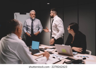 Group of colleagues in formal clothing sitting at table with computers and documents while listening to male coworkers discussing details of business strategy - Shutterstock ID 2278262623