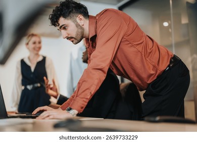 A group of colleagues interactively discussing and working together around a laptop in a contemporary open office environment, depicting teamwork and collaboration.