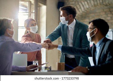 Group of colleagues wearing protective face masks and fist bumping while having business meeting during coronavirus pandemic. 