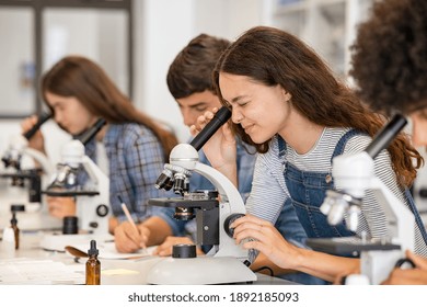 Group of college students performing experiment using microscope in science lab. University focused student looking through microscope in biology class. High school girl examine samples during lecture