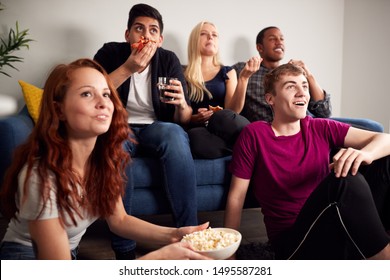 Group Of College Students In Shared House Watching TV And Eating Popcorn