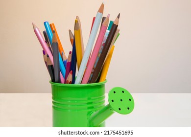 Group Of Colored Crayons In A Green Pen Holder In The Shape Of A Watering Can. Education Concept On White Background.