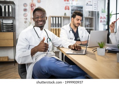 Group Of Competent Doctors With Laptops And Tablets Having Meeting At Medical Office. International Specialists Sharing With Knowledge. African Male Doctor Shows Thumb Up