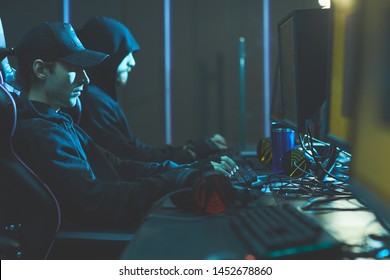 Group of concentrated hackers in black hoodies sitting in line at table and breaking into classified data