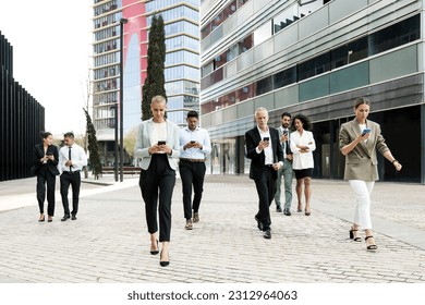 Group of confident business people walking the street using their phones. Diverse team of focused businesswoman and businessman walking outside while texting on their smartphones. - Powered by Shutterstock