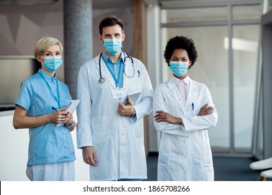 Group Of Confident Healthcare Workers Wearing Face Masks While Standing In A Hallway At Medical Clinic And Looking At Camera. 