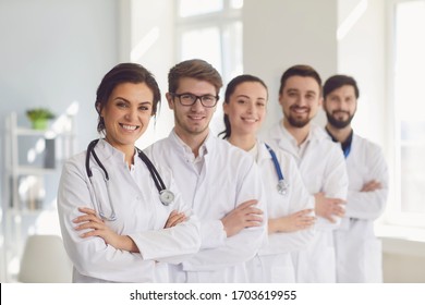 A group of confident practicing doctors in white coats are smiling against the backdrop of the clinic.
