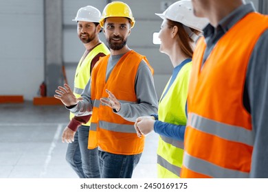 Group of confident, successful, happy managers wearing hard hats and vests, walking through large warehouse, discussing cooperation, distribution, planning. Teamwork concept - Powered by Shutterstock