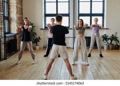 Group of contemporary teenage girls and guy looking at dance instructor during repetition of vogue dancing in spacious studio - Powered by Shutterstock