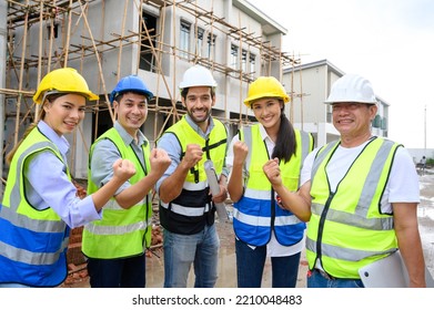 Group Of Contractors, Engineers And Formats In Safety Vests With Helmets Hands Up To Work Together To Successfully Complete A Construction Project On Construction Site. Cooperation And Success Concept