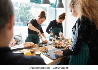 group of cooks, friends or colleagues cut ingredients cook together and prepare dinner at a wooden table in a kitchen or restaurant - Powered by Shutterstock