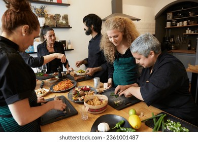 group of cooks, friends or colleagues cut ingredients cook together and prepare dinner at a wooden table in a kitchen or restaurant - Powered by Shutterstock