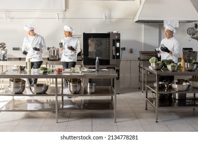 Group of cooks using phones and drinking coffee during a break in the restaurant kitchen. Professional staff resting after work in kitchen. Multiracial team of cooks indoors - Powered by Shutterstock