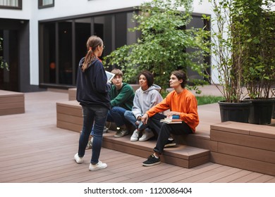 Group of cool students sitting and preparing for lesson while studying together in courtyard of university