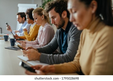 Group of coworkers sitting at the table in the office and using cellphones - Shutterstock ID 1795028698