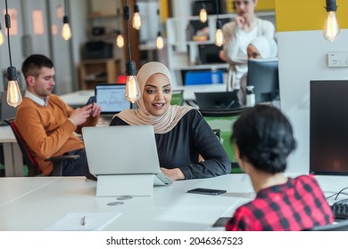 Group of coworkers, teammates helping their new African American, black, muslim colleague wearing hijab to integrate into the modern company. Multiethnic colleagues in a modern startup company. - Shutterstock ID 2046367523