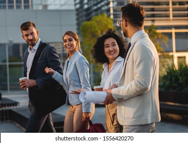 Group Of Coworkers Walking Outside In Front Of Office Buildings Discuss About Business Plan.