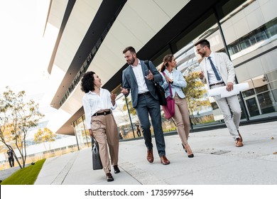 Group Of Coworkers Walking Outside In Front Of Office Buildings Discuss About Business Plan.