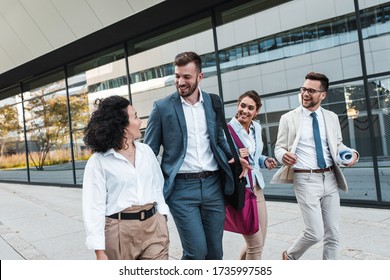 Group of coworkers walking outside in front of office buildings discuss about business plan. - Powered by Shutterstock