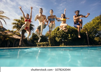 Group Of Crazy Young People Jumping Into A Swimming Pool. Friends Having Fun At A Holiday Resort.