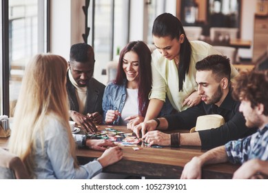 Group of creative friends sitting at wooden table. People having fun while playing board game.