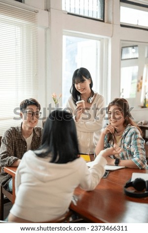 A group of creative and smart young Asian students are discussing work, sharing their ideas for a project, and having a meeting at a co-working space cafe. Teamwork, friendship, co-working, startups