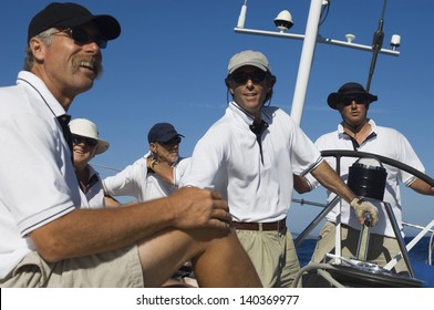 Group of crew members relaxing on yacht deck by helm against clear blue sky