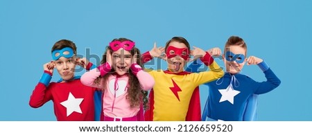 Group of cute children in colorful superhero costumes looking at camera and grimacing against bright blue background