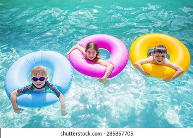 Group Of Cute Kids Playing On Inflatable Tubes In A Swimming Pool On A Sunny Day