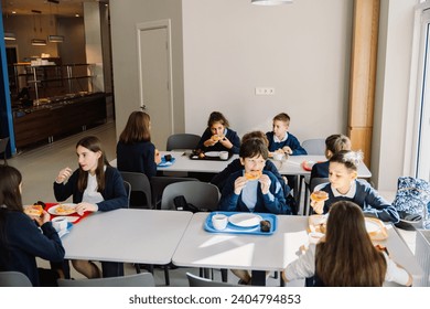 Group of cute primary school children wearing uniform eating pizza while sitting in school cafeteria - Powered by Shutterstock