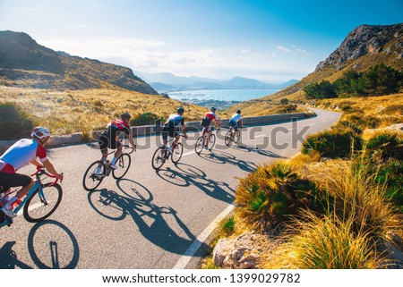 Group of cyclist ride together on road bicycles in beautiful nature. Sunset light, sea in background.