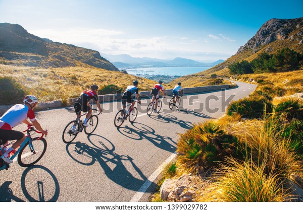 Group of cyclist ride\
together on road bicycles in beautiful nature. Sunset light, sea in\
background.