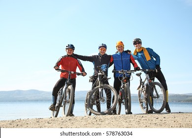 Group Of Cyclists On A Shore Of A Mountain Lake. Team Outdoors. Mountain Bike