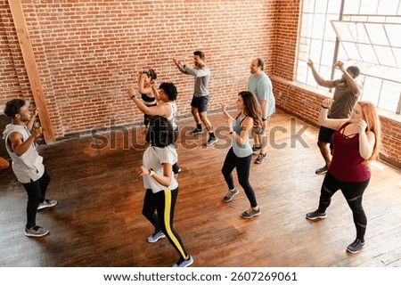 Group dance class in a studio with brick walls. Diverse men and women enjoying a lively workout. Dance class energy and fun in a bright studio setting. Diverse people exercising in fitness class.