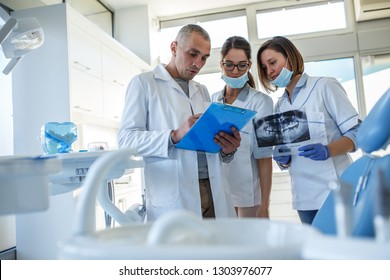 Group Of Dentists Examining X-ray Image Of Patients Teeth. Standing In New Bright Dentist Office.