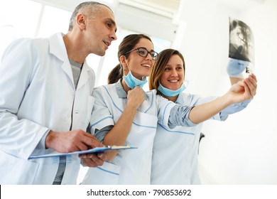 Group Of Dentists Examining X-ray Image Of Patients Teeth. Standing In New Bright Dentist Office.