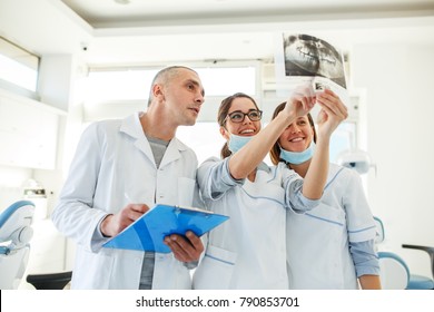 Group Of Dentists Examining X-ray Image Of Patients Teeth. Standing In New Bright Dentist Office.