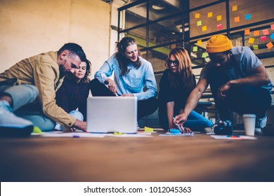 Group Of Designers Making Researchers During Brainstorming Session Sitting On Floor Talking , Team Of Creative Co-workers Using Technology And Papers Planning Startup Collaborating On Strategy