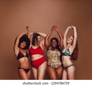 Group of different size women in bikinis dancing together. Multi-ethnic women in swimwear enjoying themselves in studio.