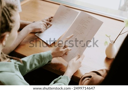 Group of diners examining menu choices in cozy restaurant beside bright window, focusing on different options and discussing their preferences