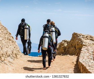 Group Of Divers With Equipment For Diving Go To The Sea Against The Blue Sky And Clouds In Egypt Dahab