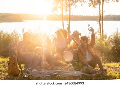 Group of diverse adults and children, mixed genders and ages, sharing a meal by a lake, surrounded by nature, in the warm glow of the evening sun. Family and Friends Enjoying Lakeside Picnic at - Powered by Shutterstock