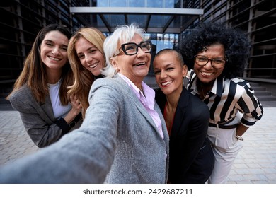 Group of diverse business formal women taking selfie with phone looking smiling at frontal camera. Happy cheerful photo only female people co-workers outdoor. Gray mature lady looking up joyful  - Powered by Shutterstock