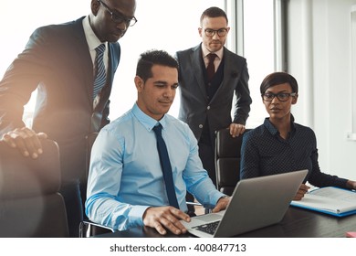 Group Of Diverse Business People In Formal Clothing Inside Their Office Discussing Or Looking At Information On A Laptop Computer