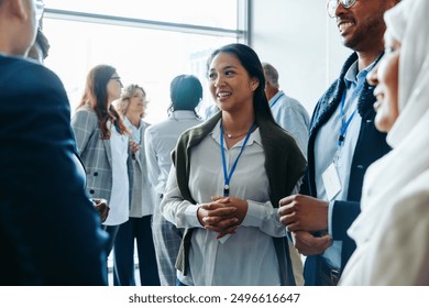 Group of diverse business professionals, businessmen and businesswomen, networking at a conference event. They are smiling, conversing, and engaging in discussions during a daytime seminar.