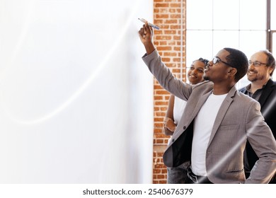 Group of diverse business professionals in a meeting. Man writing on whiteboard. Diverse team, collaboration, brainstorming. Office setting, teamwork, business meeting and brainstorming concept. - Powered by Shutterstock