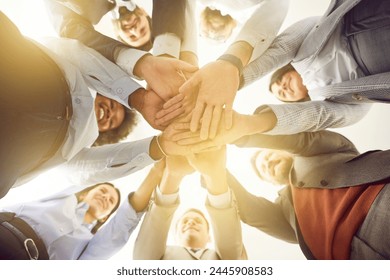 Group of diverse business professionals is shown from a low angle, standing in a circle and stacking their hands together. Symbolize team unity, teamwork, and collaboration in a business setting - Powered by Shutterstock