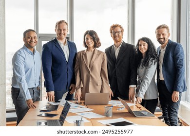 A group of diverse business professionals stand in a modern office space, smiling for a photograph. The team consists of both men and women. They are dressed in business attire - Powered by Shutterstock