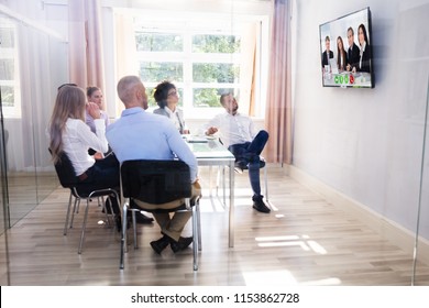 Group Of Diverse Businesspeople Looking At Television While Video Conferencing In Boardroom